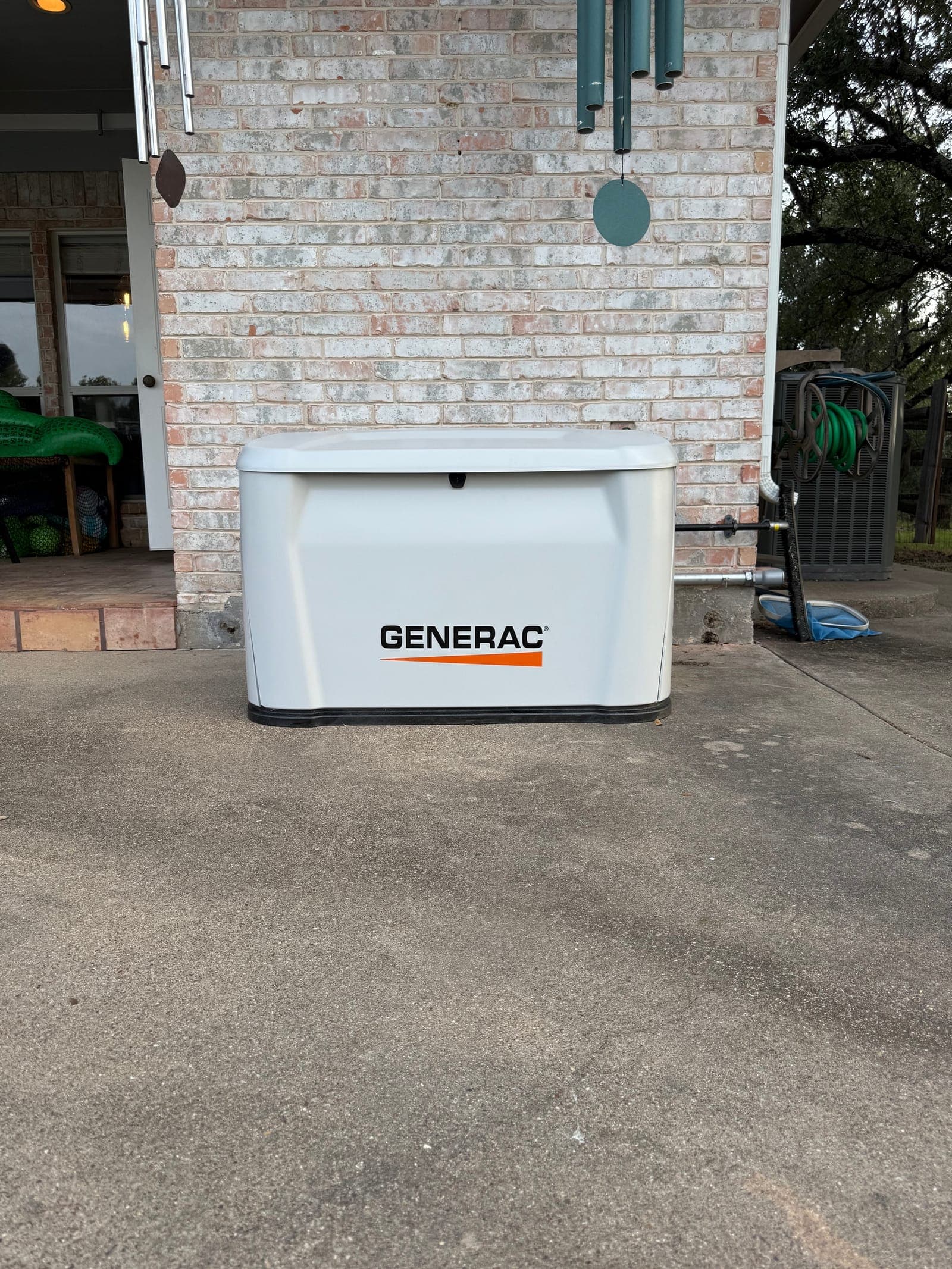 A finished Generac home standby generator on its pad beside a brick wall, with the gas line and conduit run in along the wall.